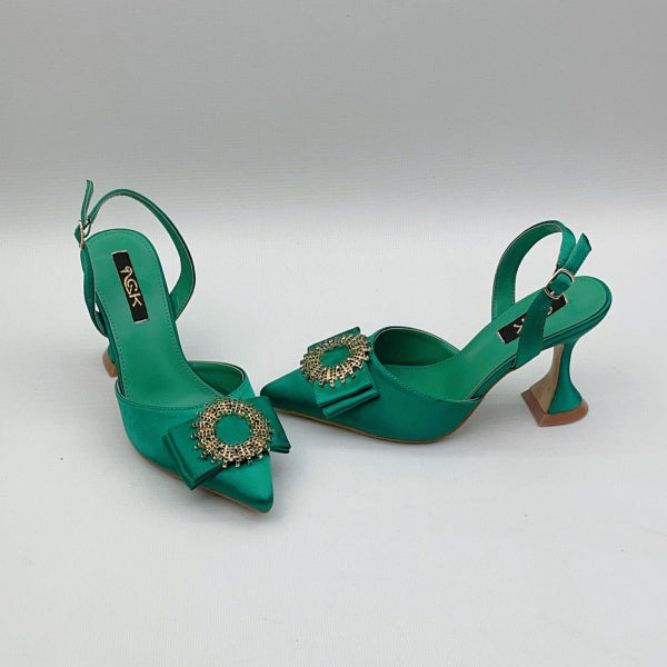 Green high-heeled shoes with decorative elements on a light gray background