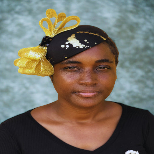 Woman wearing a black headband with gold decorative elements against a blurred natural background