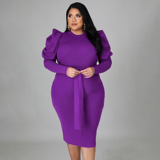 Woman wearing a purple dress with puffed sleeves against a gray background